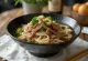 Mangkuk berisi mi udon tebal dengan irisan daging sapi